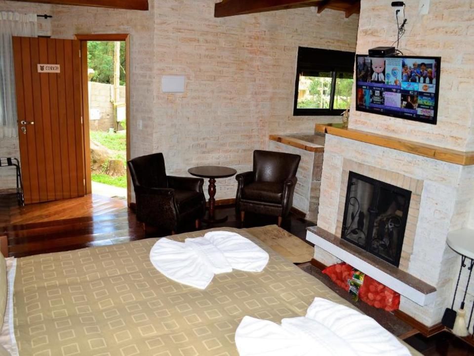 Sala de estar aconchegante com lareira, poltronas, TV e porta de madeira aberta para um jardim.