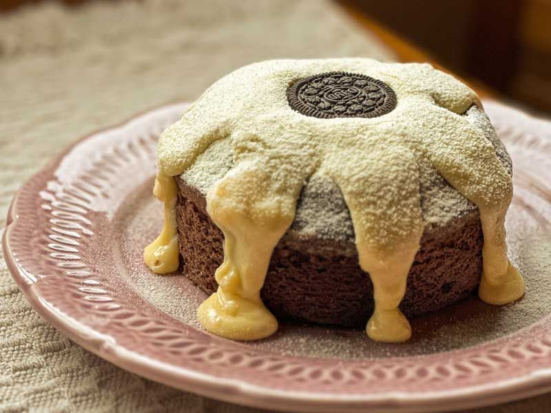 Bolo vulcão de chocolate com cobertura de glacê branco servido em um prato rosa estampado.