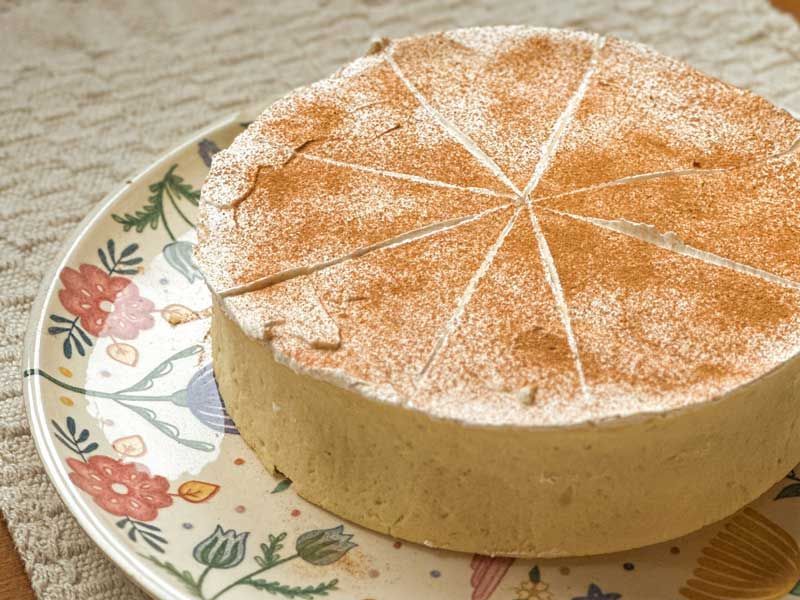Bolo redondo polvilhado com canela, servido em um prato florido sobre uma superfície bege.