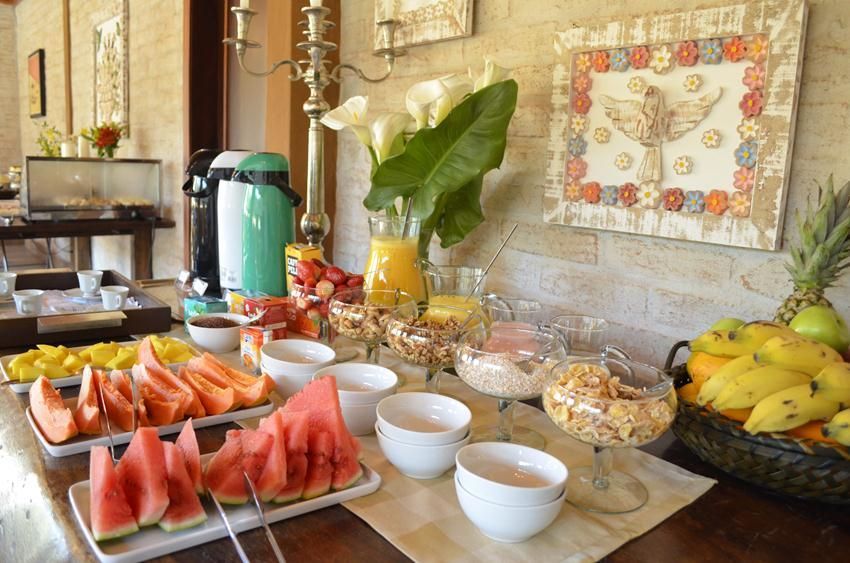 Buffet de café da manhã com pratos de frutas, tigelas de iogurte e bebidas em uma mesa em uma sala iluminada.