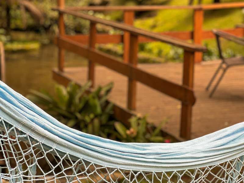 Rede branca em primeiro plano com vista para um caminho de madeira no jardim e plantas.