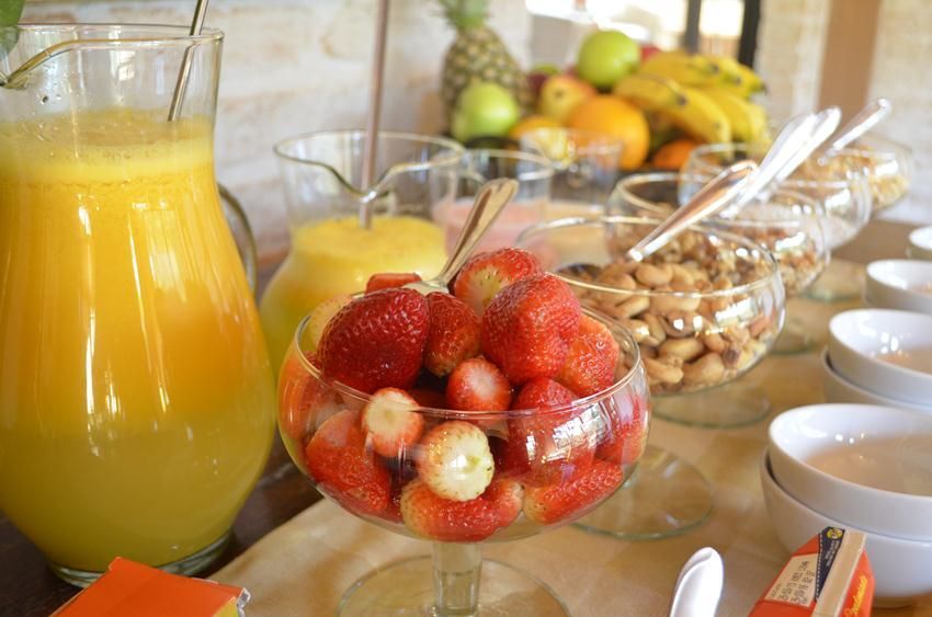 Mesa de café da manhã com suco de laranja, tigela de morangos, frutas e tigelas de cereais.