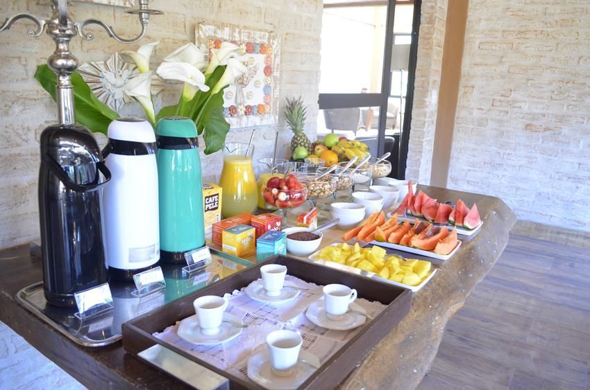 Buffet de café da manhã com cafeteiras, doces, frutas e sucos em uma mesa comprida.