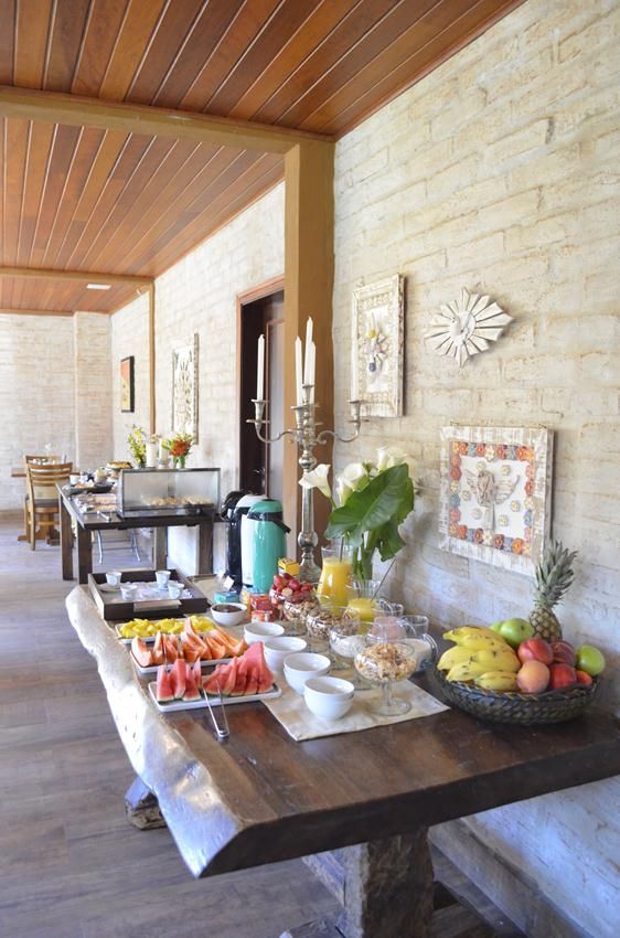 Mesa de buffet com frutas e doces em um pátio externo coberto ao lado de um muro de pedra.