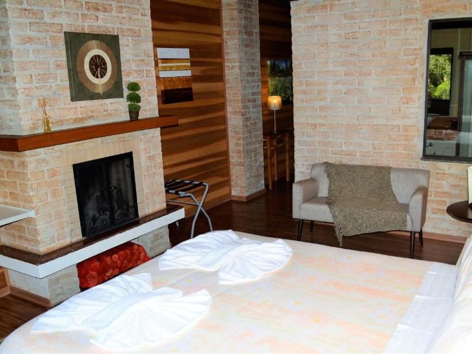 Quarto de hotel aconchegante com lareira de tijolos, cama, poltrona e porta de madeira em tons quentes.