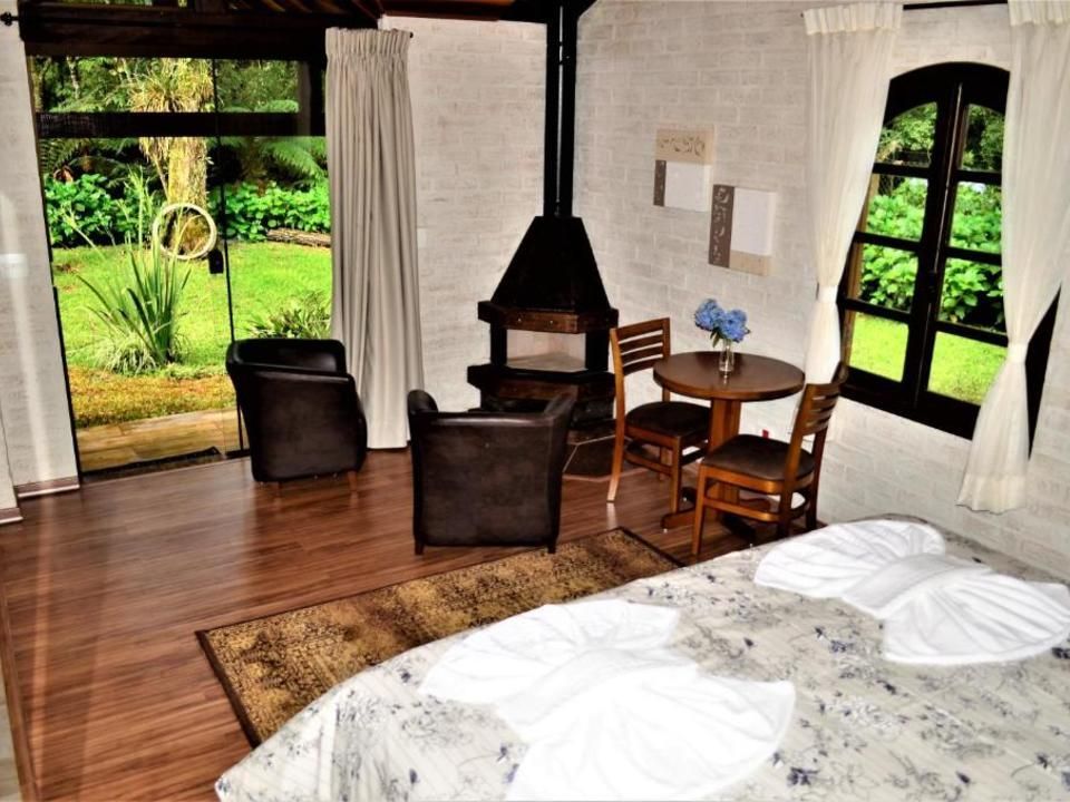 Quarto aconchegante com duas camas de solteiro, lareira, piso de madeira e portas abertas para um jardim exuberante.