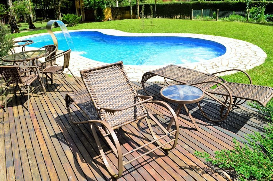 Deck de madeira com espreguiçadeiras ao lado de uma pequena piscina azul em um quintal ensolarado.