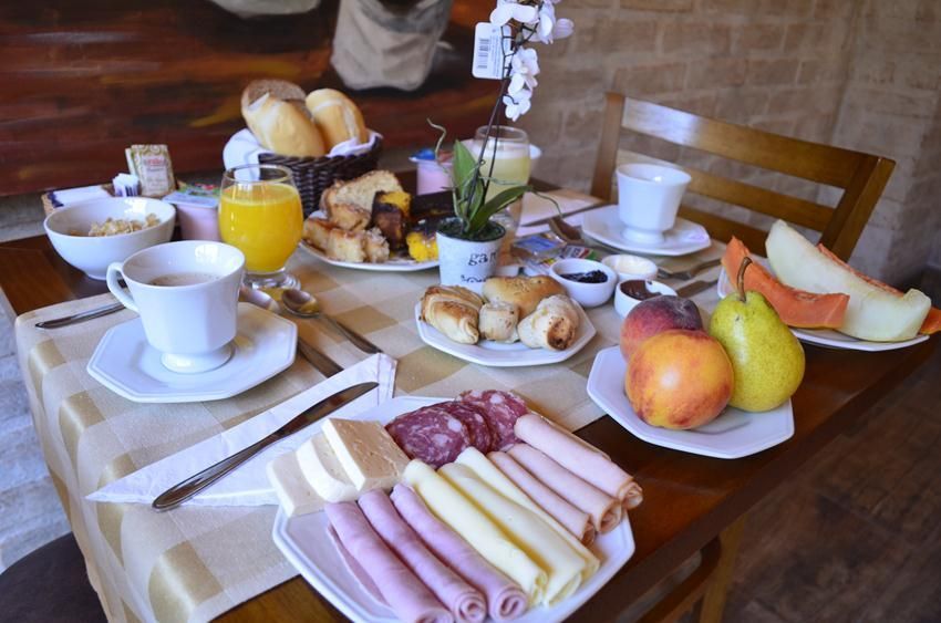 Café da manhã servido em uma mesa de café com café, suco de laranja, doces, frutas e guardanapos dobrados.