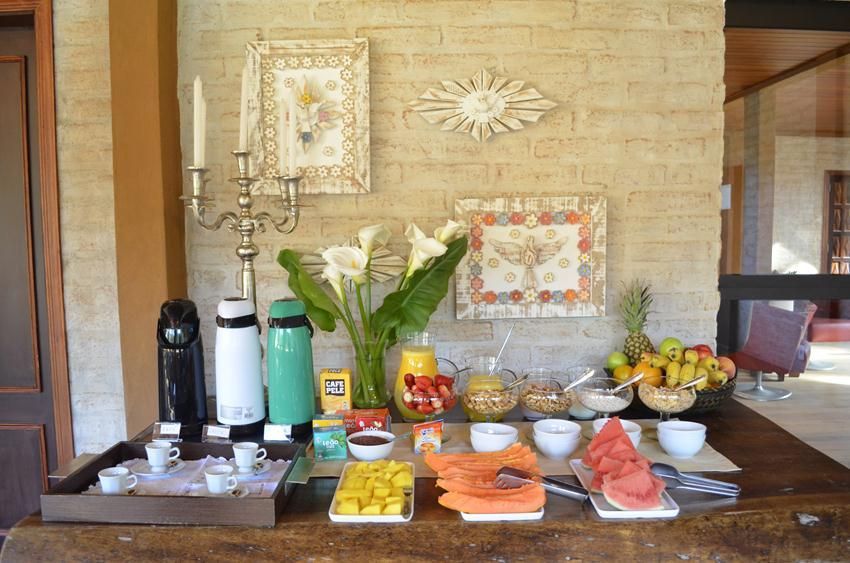 Mesa de buffet com frutas, doces, bebidas e flores encostada em uma parede de pedra.