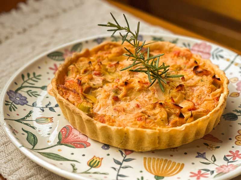 Tarte dourada e salgada servida num prato florido, decorada com alecrim.