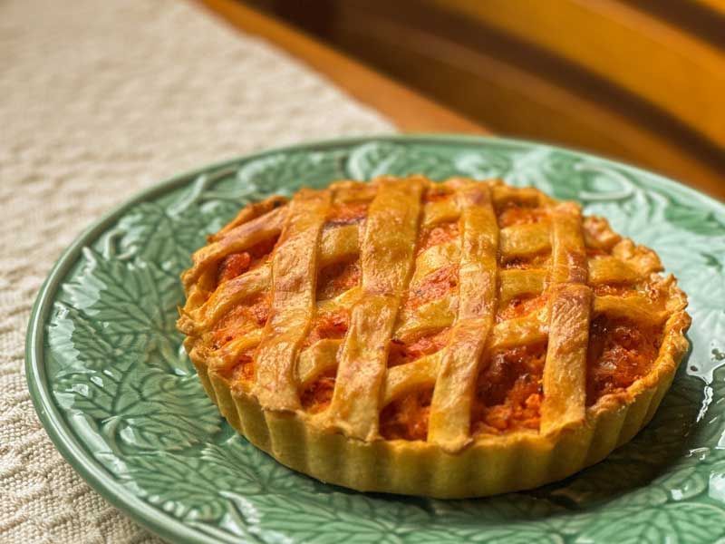 Tarte de frutas com cobertura de treliça servida num prato verde sobre uma mesa de madeira.
