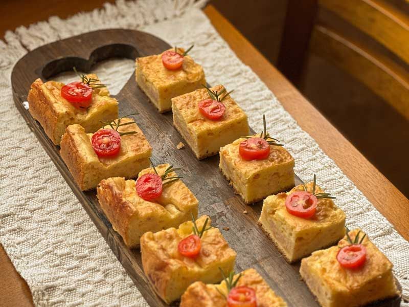 Fileiras de torradas pequenas cobertas com tomates-cereja dispostas em uma tábua de madeira.