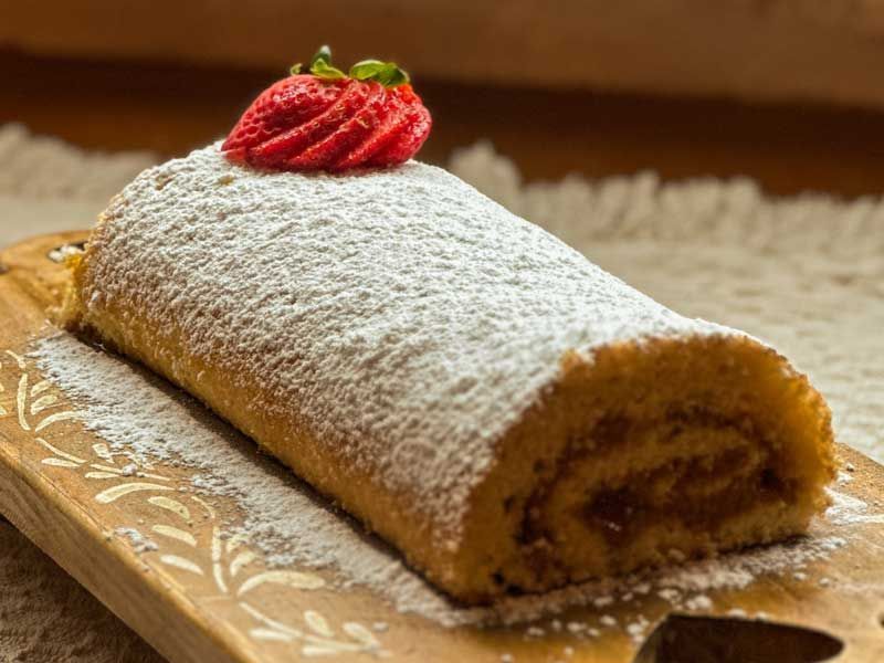 Bolo rocambole de morango polvilhado com açúcar de confeiteiro em um prato decorativo.