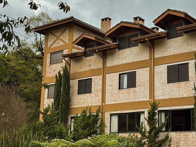 Casa moderna de três andares com frontões revestidos de madeira e área verde na frente.