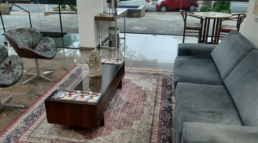Uma área de estar com um sofá cinza, poltronas estampadas e uma mesa de centro de madeira escura sobre um tapete estampado perto de uma janela.