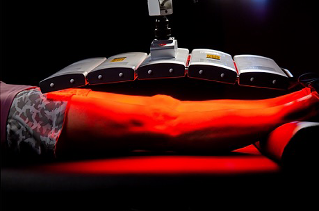 A person is laying on a bed with red lights on their legs.