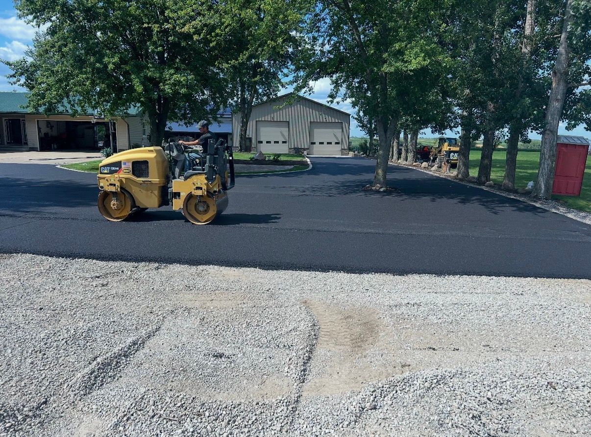 Asphalt driveway between brick building and gray-sided house. Wet surface, sidewalk in foreground.