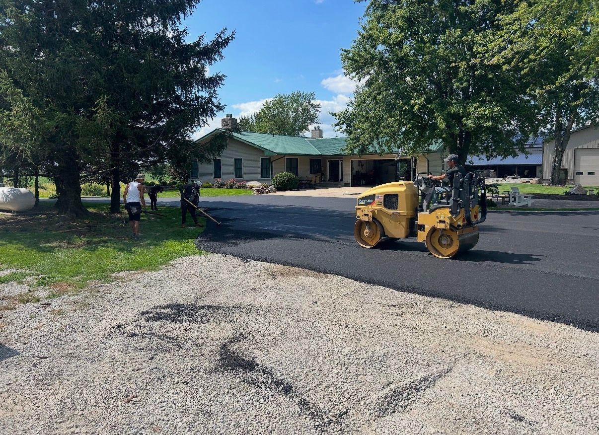 Asphalt driveway between brick building and gray-sided house. Wet surface, sidewalk in foreground.