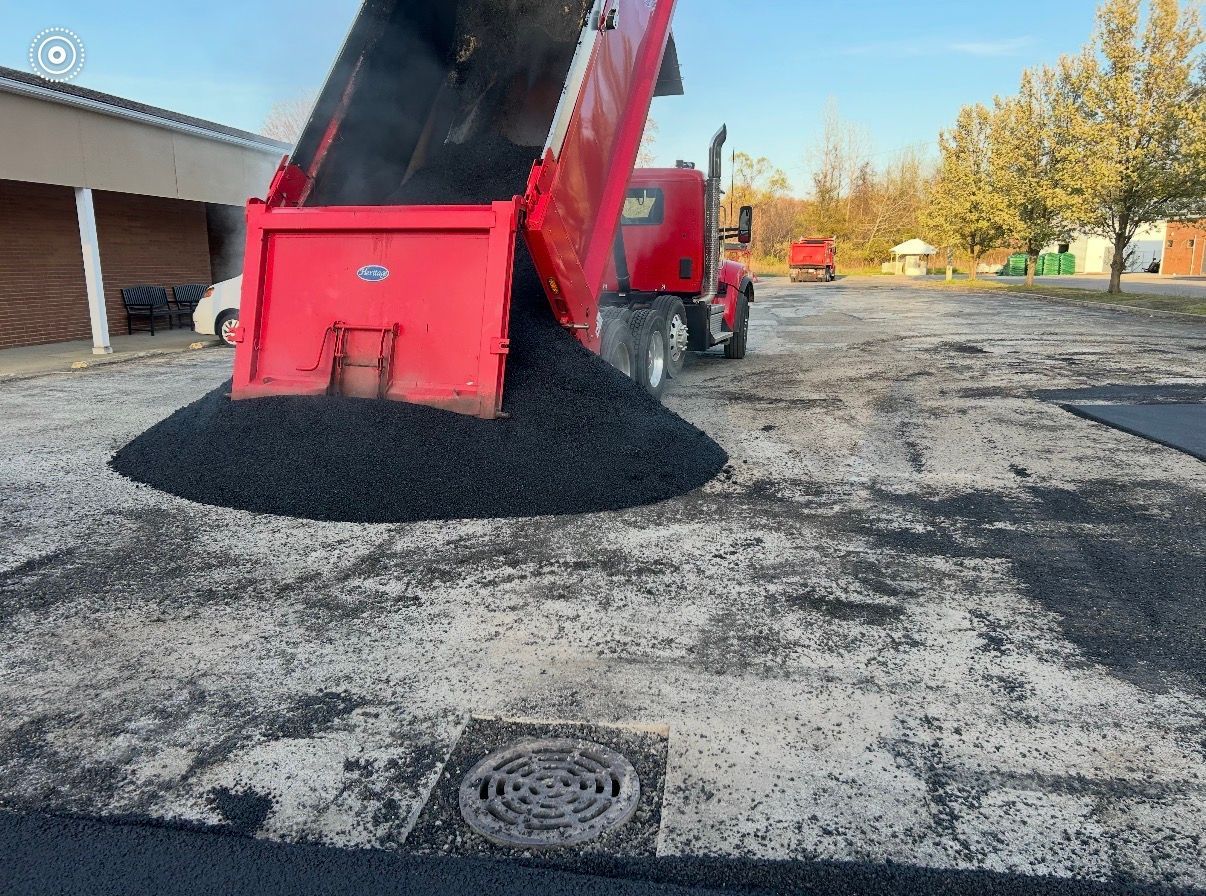 Newly paved black asphalt driveway in front of a blue-gray house with a white garage door, yellow markings, and a white sign.