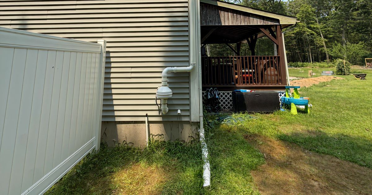Backyard beside beige house, with white fence, screened porch, grass, and a blue-and-green toy cart.