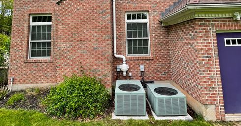Brick house exterior with two HVAC units beneath windows and a purple door on the right