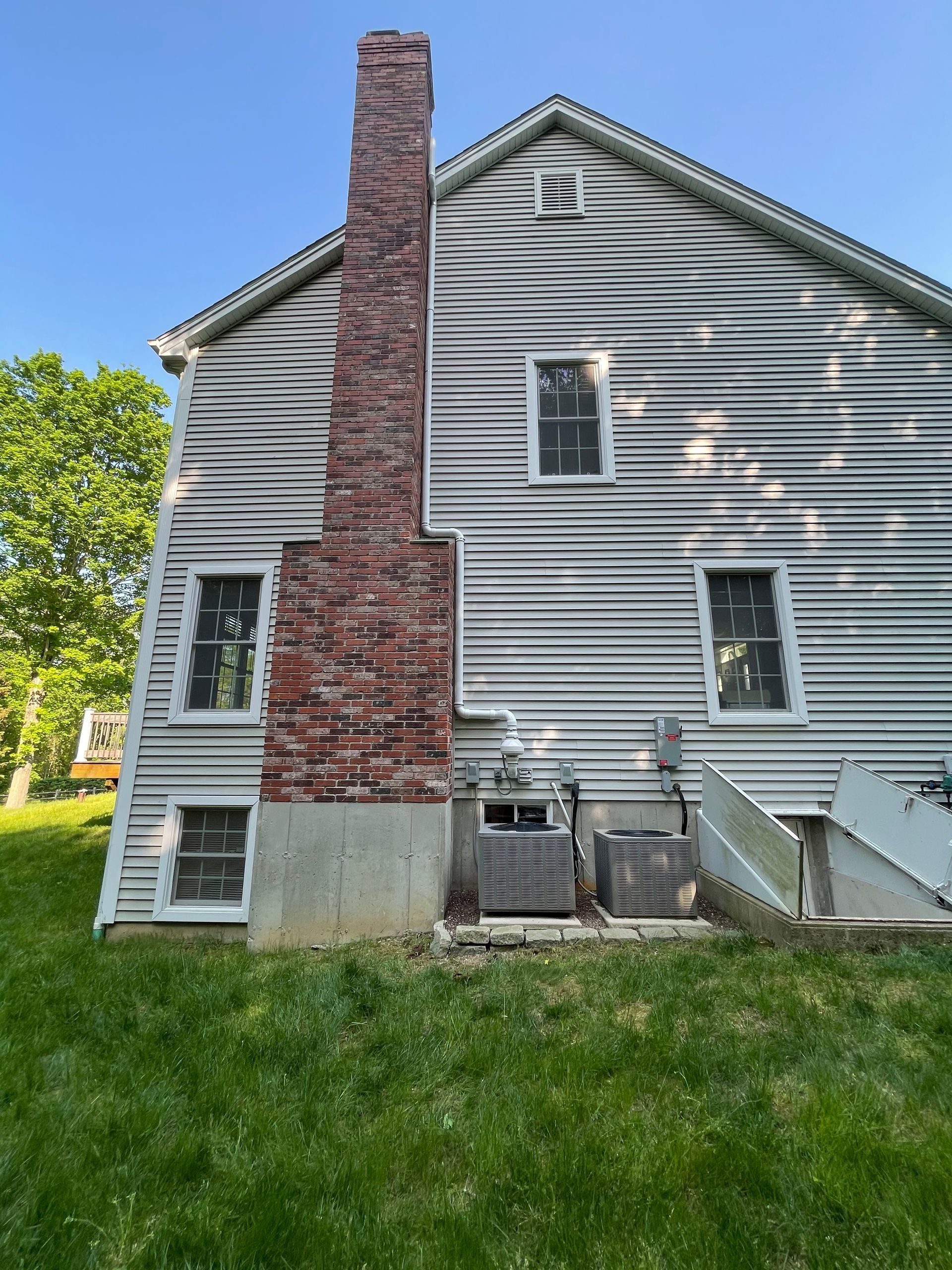 Gray-sided house with a red brick chimney and green lawn in front.