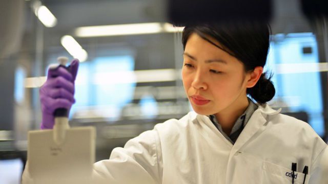 Scientist in a lab coat pipetting liquid into a tube in a laboratory