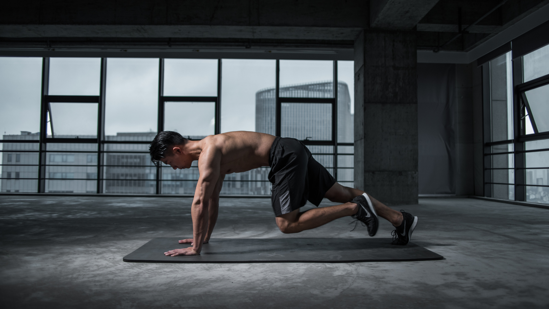 Man exercising in a plank position on a mat in a gym with large windows