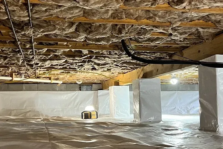 Partially finished basement with exposed insulation, white wrapped support columns, and plastic floor covering