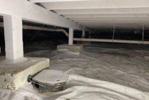 Crawlspace under a house with white beams, insulation, and exposed ductwork in low light