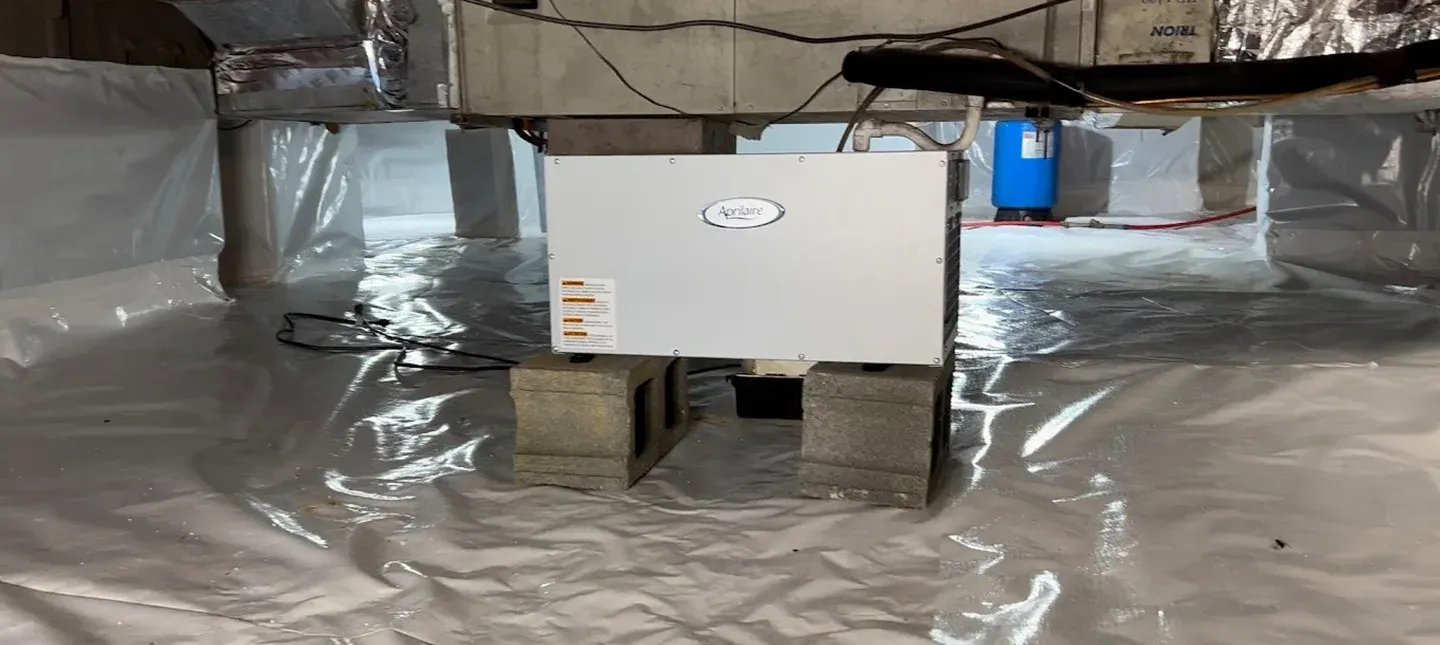 Insulated attic with plastic vapor barrier and a white HVAC unit on cinder blocks