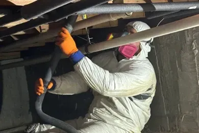 Worker in orange gloves inspecting pipes in a dark crawl space