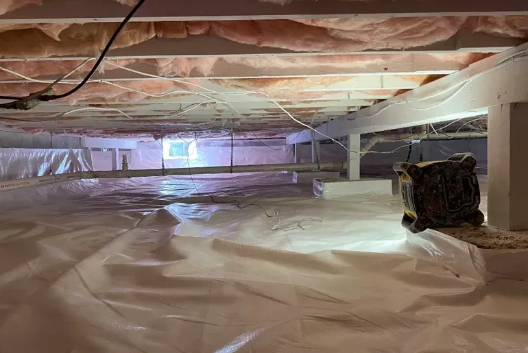 Insulated crawlspace with plastic vapor barrier, exposed joists, and a utility unit on the right