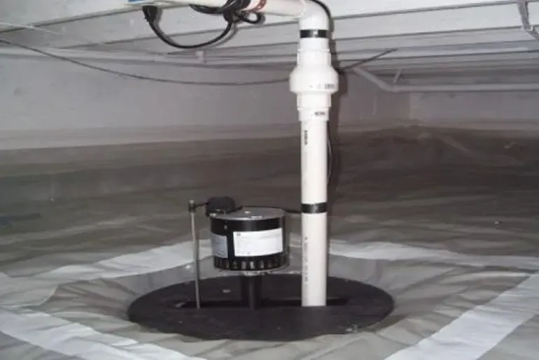 Plumbing vent and drain pipe under a sink, with a small black pump or device mounted on the floor.