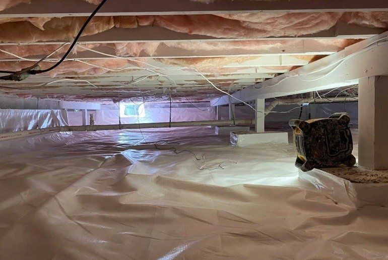 Insulated crawlspace with plastic vapor barrier, exposed joists, and a small light in the back