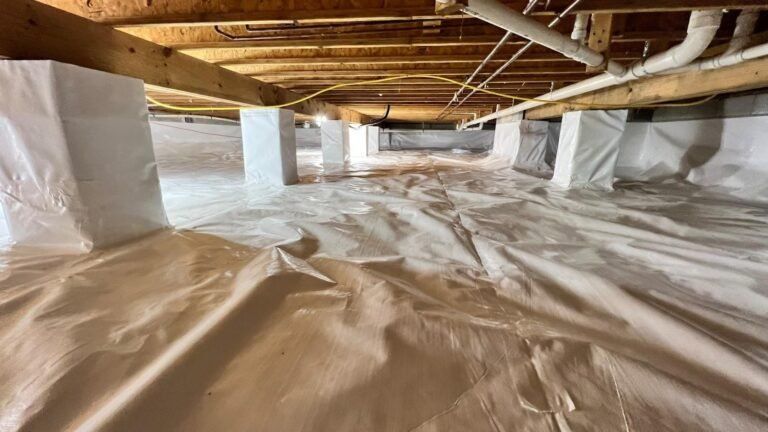 Crawl space with white vapor barrier lining the floor and exposed wooden joists overhead.
