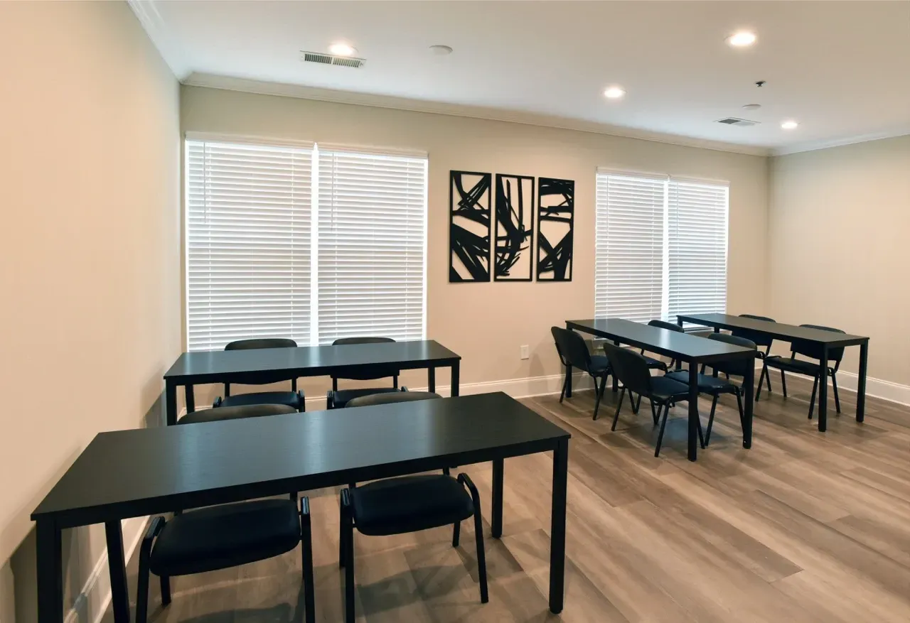 Interior community room with black tables and chairs and window blinds.