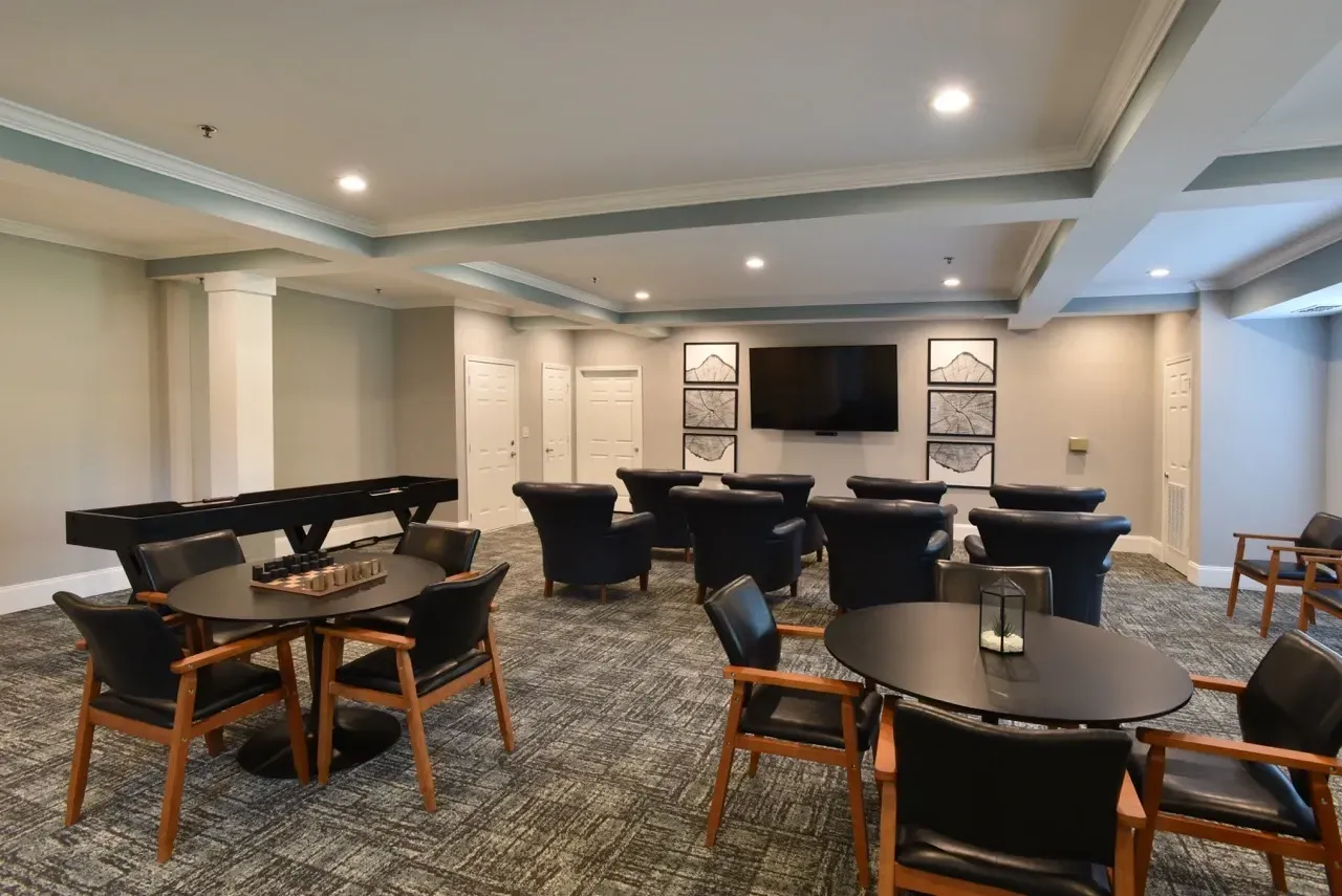 Indoor community lounge with round tables, black cushioned chairs, a wall-mounted TV, and framed art.