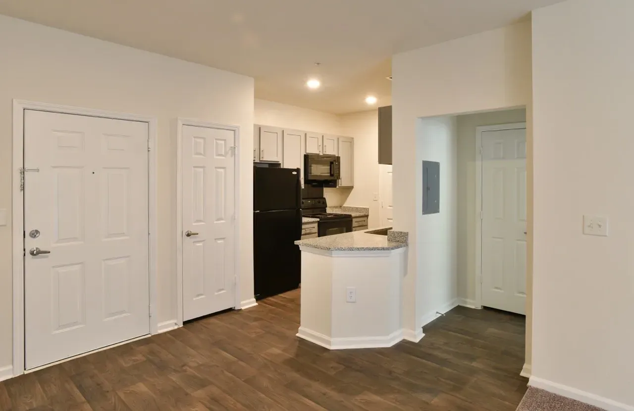 Interior view of a modern apartment kitchen with white cabinets, granite counters, and black appliances.