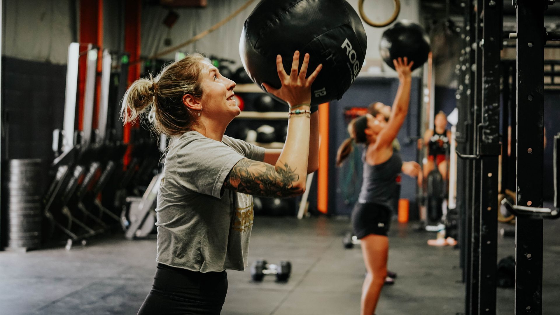 People exercising with medicine balls in a gym, one woman smiling in the foreground at the best gym in Columbus, OH.
