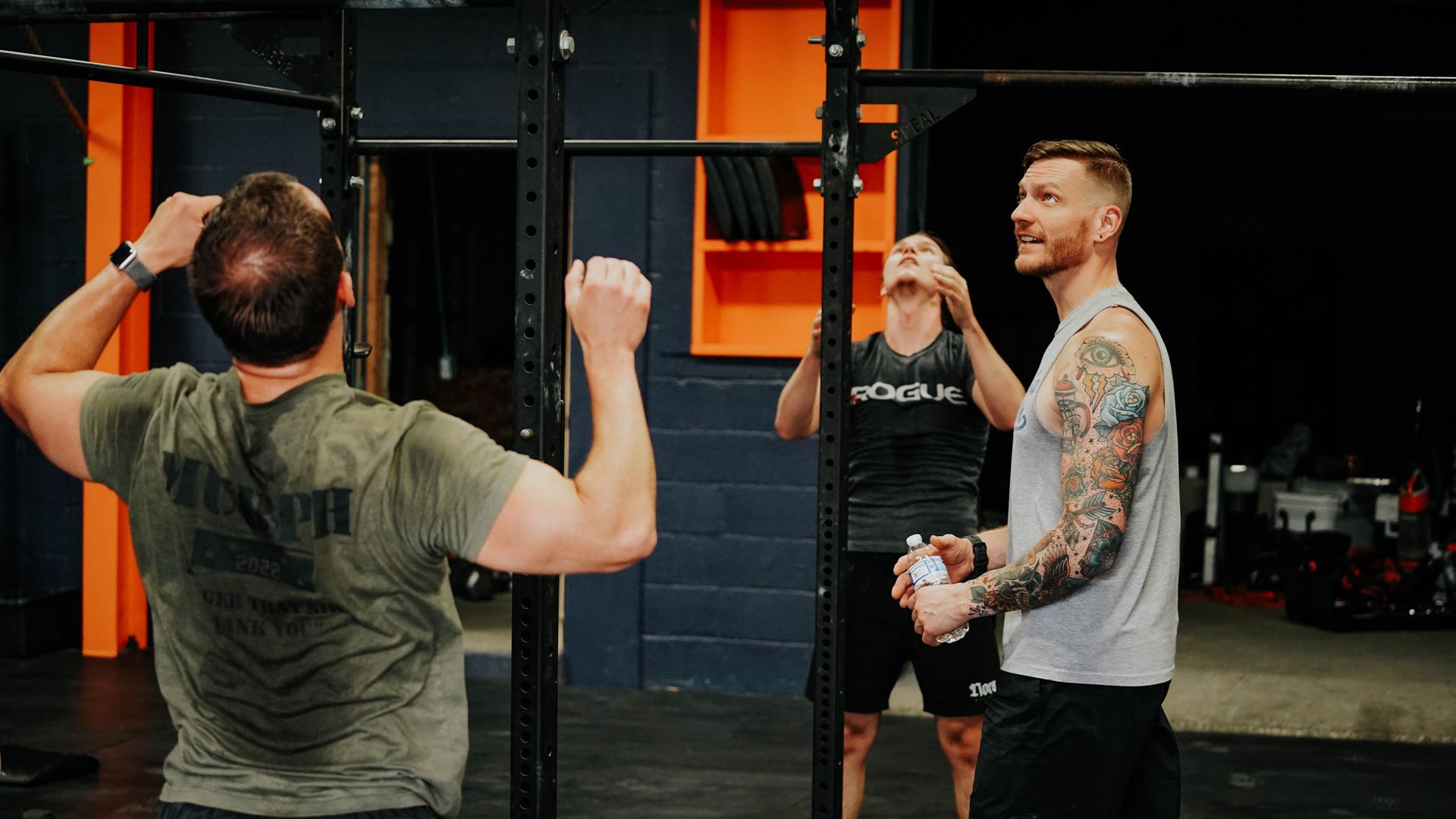 Two people talking in a gym, one facing pull-up bars while the other gestures beside them at the best gym in Columbus, OH.