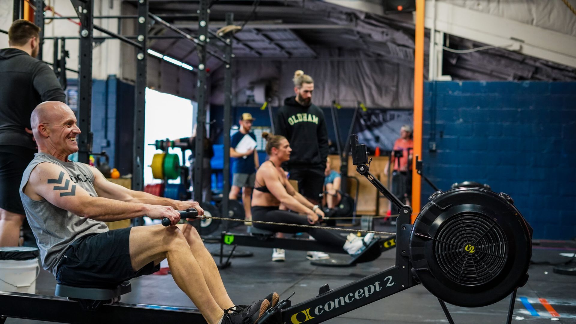People rowing on indoor rowing machines in a gym, with a large fan visible in front at the best gym in Columbus, OH.