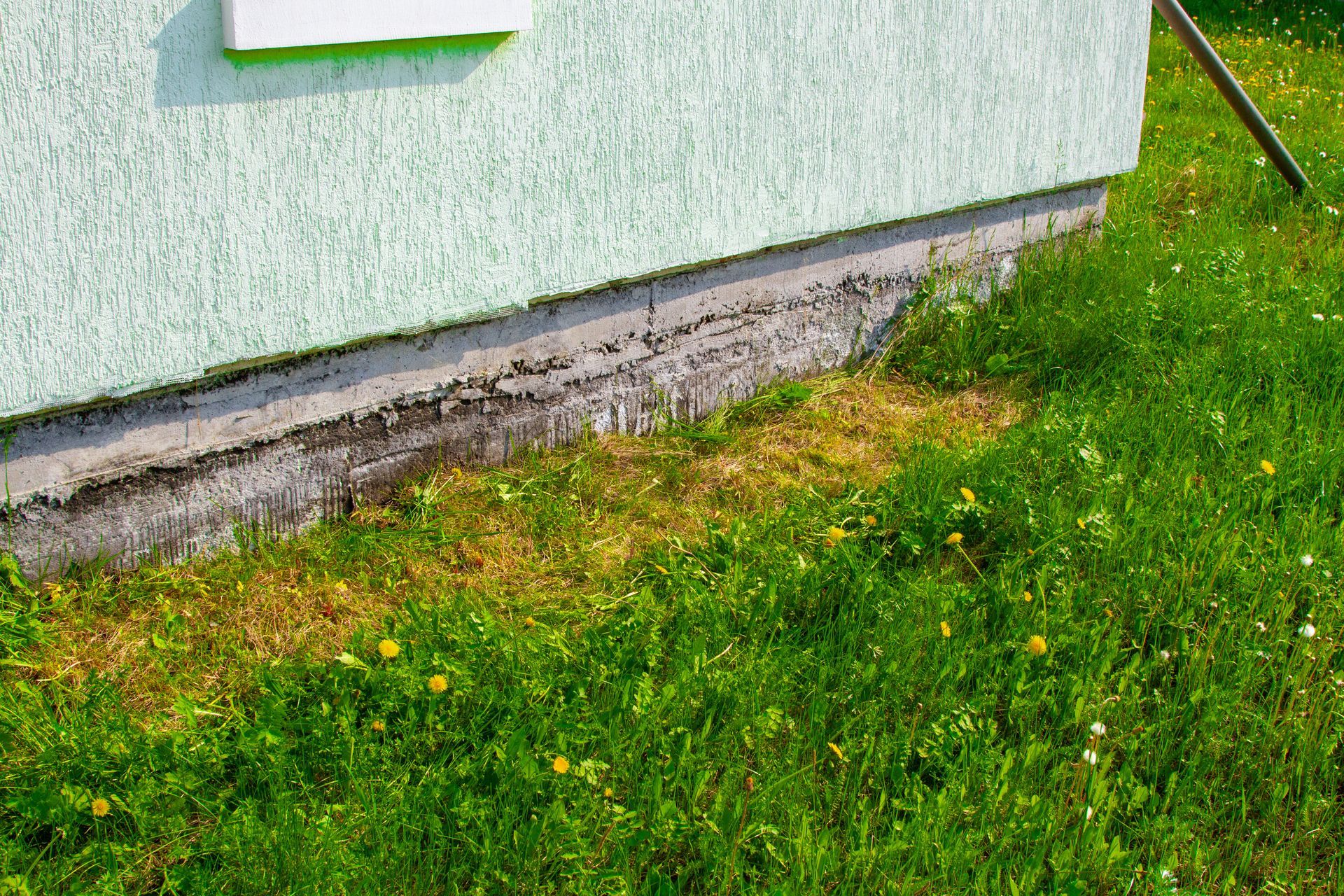 White exterior wall with a concrete foundation and patchy grass beside it