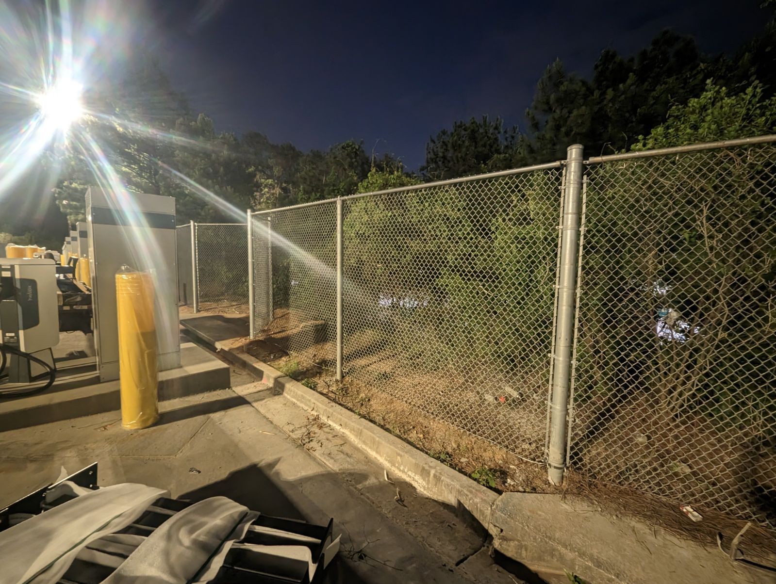 A chain link fence surrounds a parking lot at night.