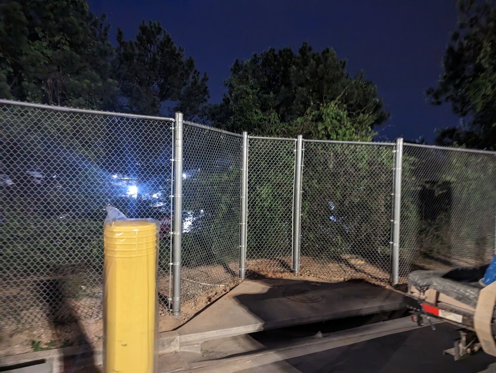 A chain link fence with a yellow pole in front of it at night.