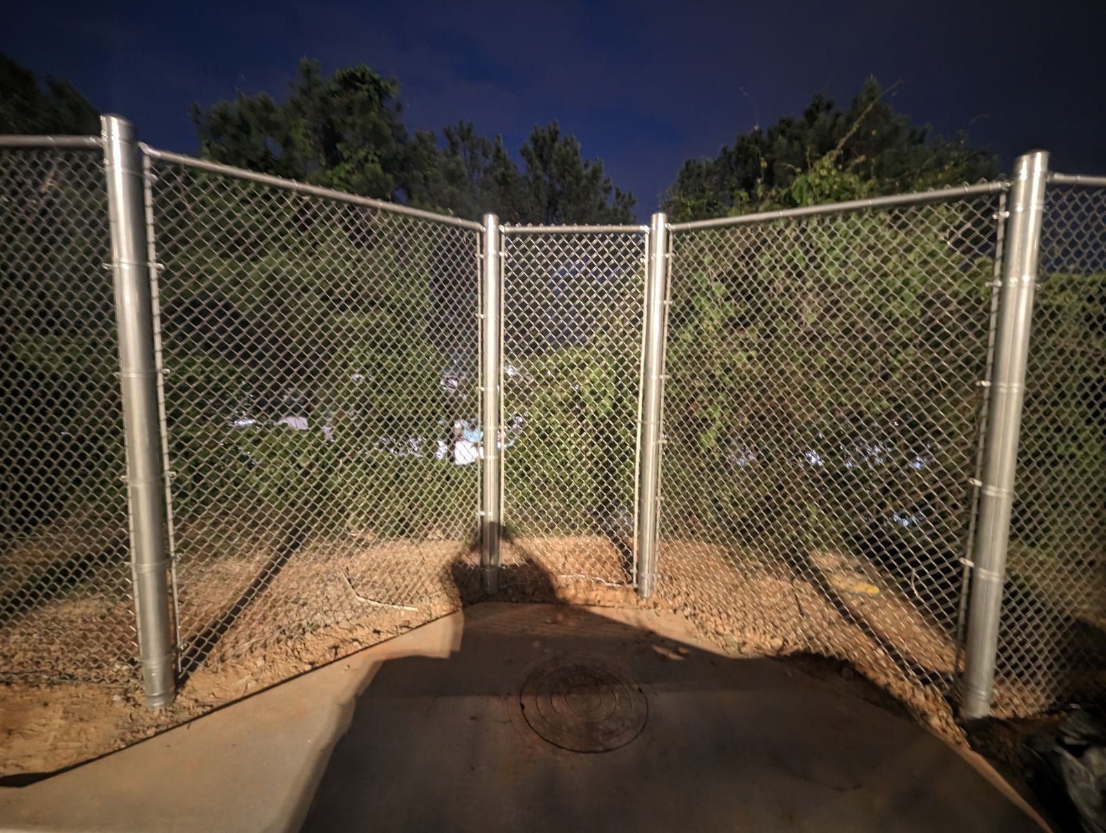 A chain link fence with trees in the background at night