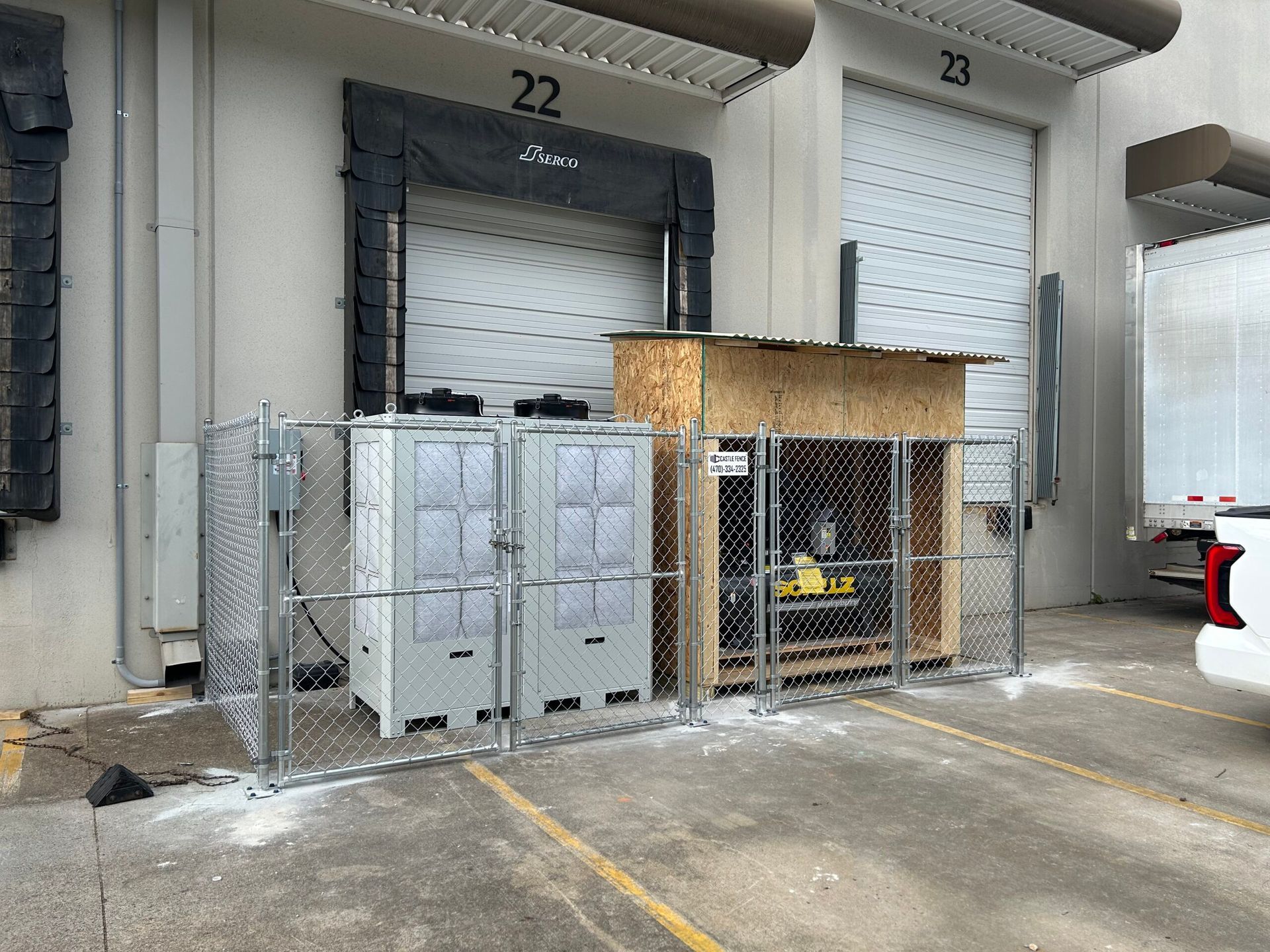 A chain link fence is surrounding a warehouse with a truck parked in front of it.