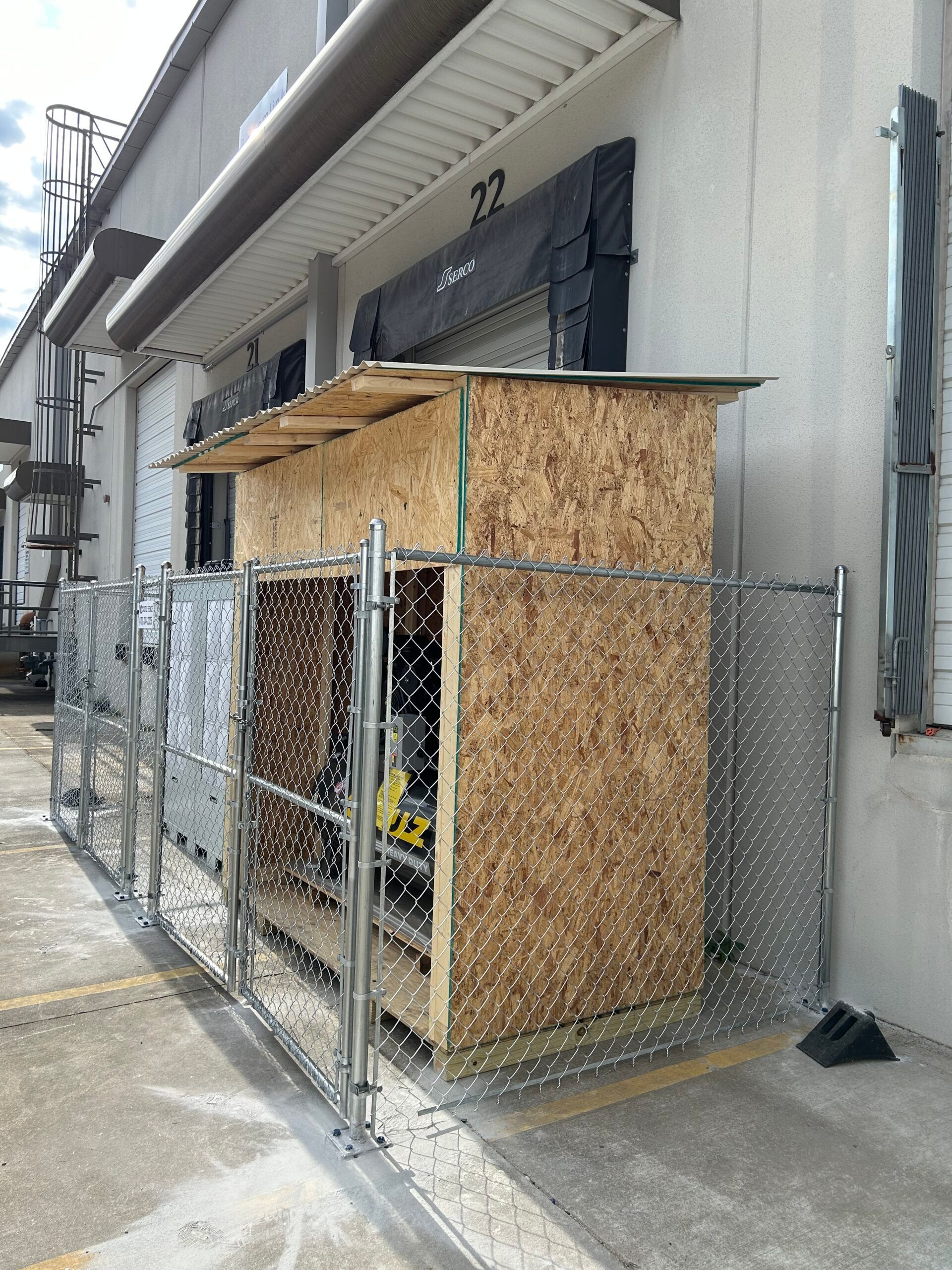 A chain link fence surrounds a building with a wooden structure in front of it.