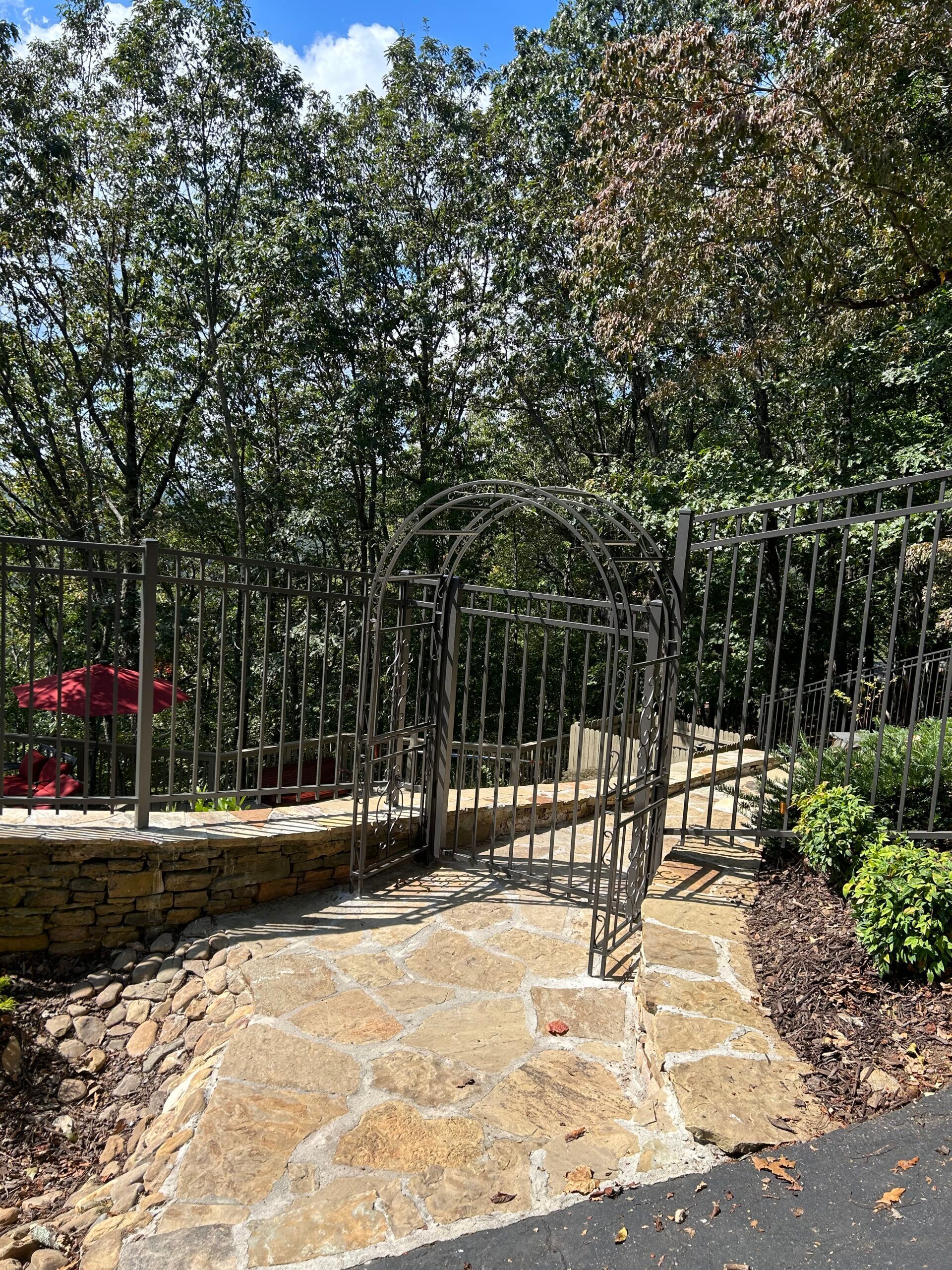 A stone walkway leading to a wrought iron gate surrounded by trees.