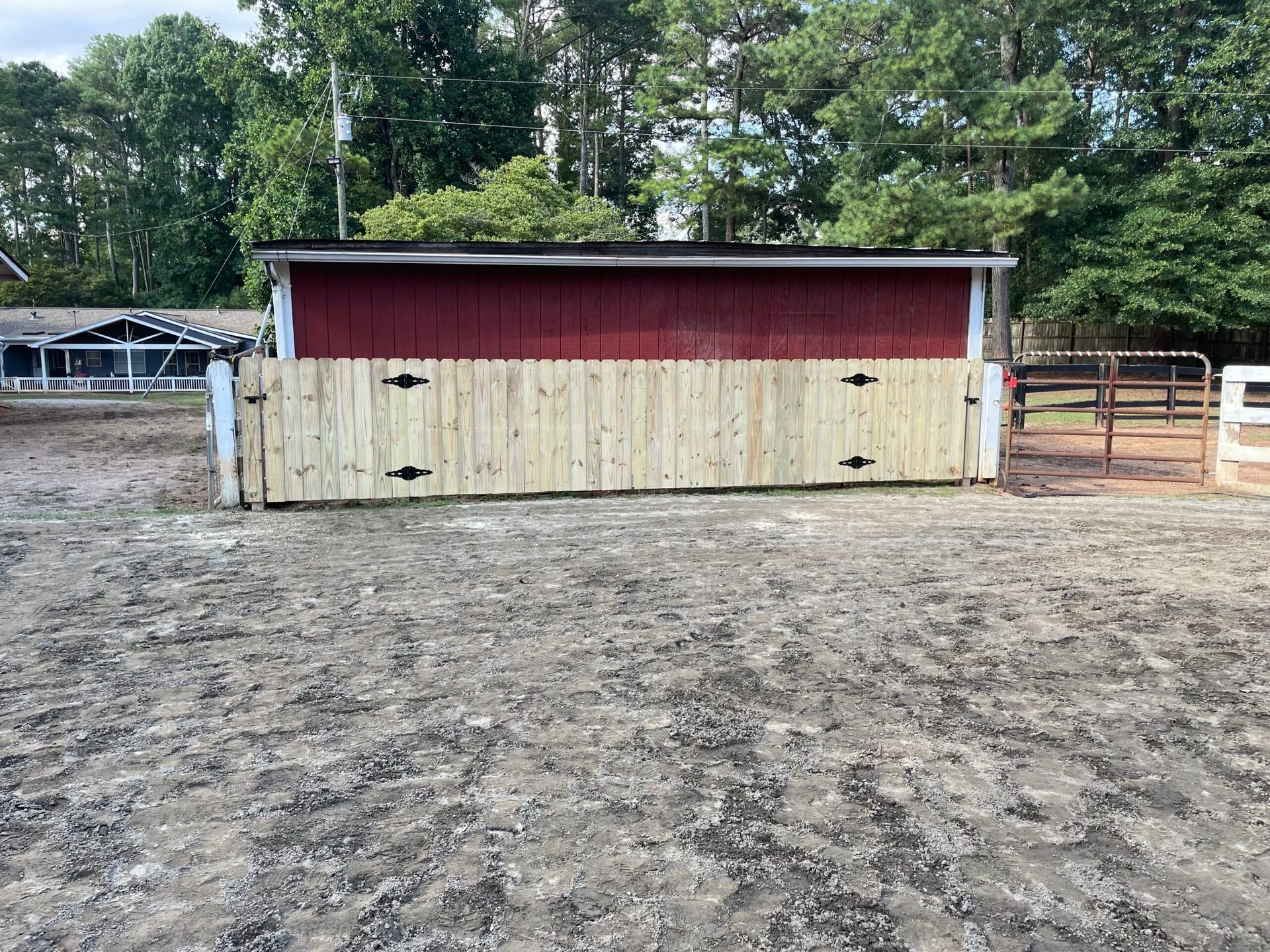 A red barn with a wooden fence around it is sitting in the middle of a dirt field.